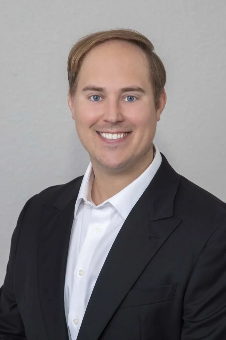Dr. Nicholas Dwan of Willow Dental in New Berlin, WI. The image shows a person wearing a black suit jacket over a white dress shirt. The background is a plain, light-colored wall.