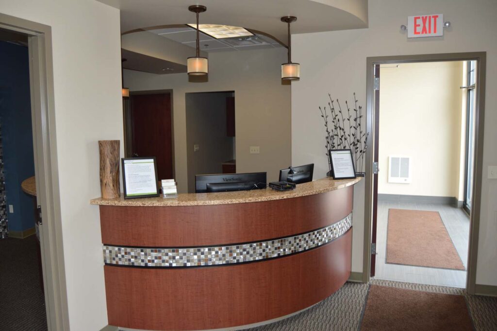 Reception area with a curved wooden desk, granite countertop, mosaic accents, and pendant lighting; professional and welcoming atmosphere.